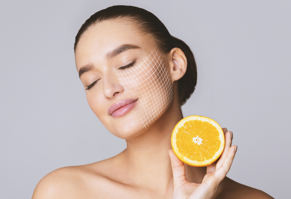 Vitamin C for skin. Delighted young pretty woman with closed eyes holding orange half