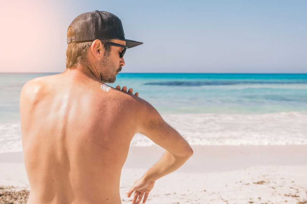 Man applying sun protection cream on his shoulder at the beach