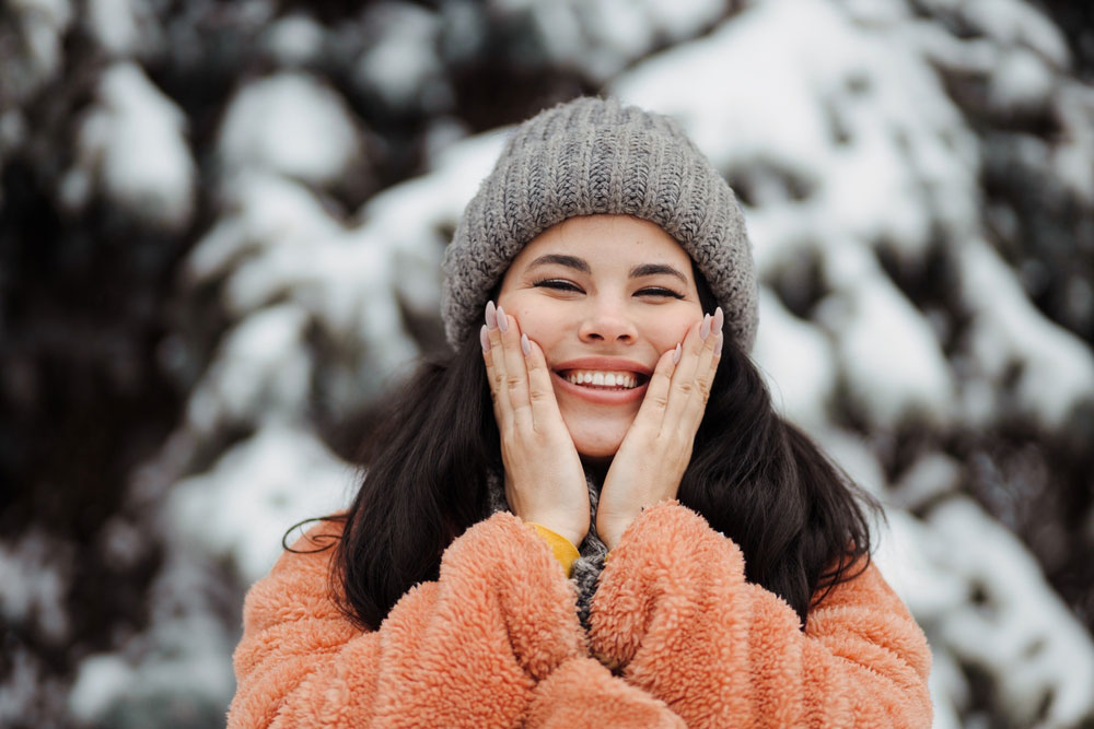 Happy pretty young woman using a skin protection cream in winter