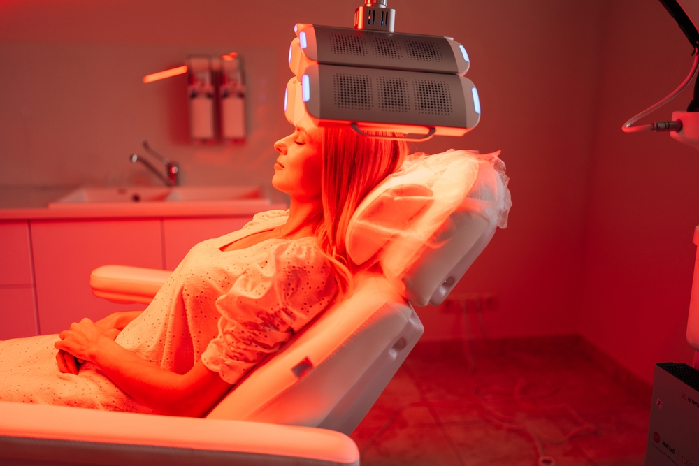 Side view portrait of blonde female lying on procedure chair having LED red light hair photodynamic therapy