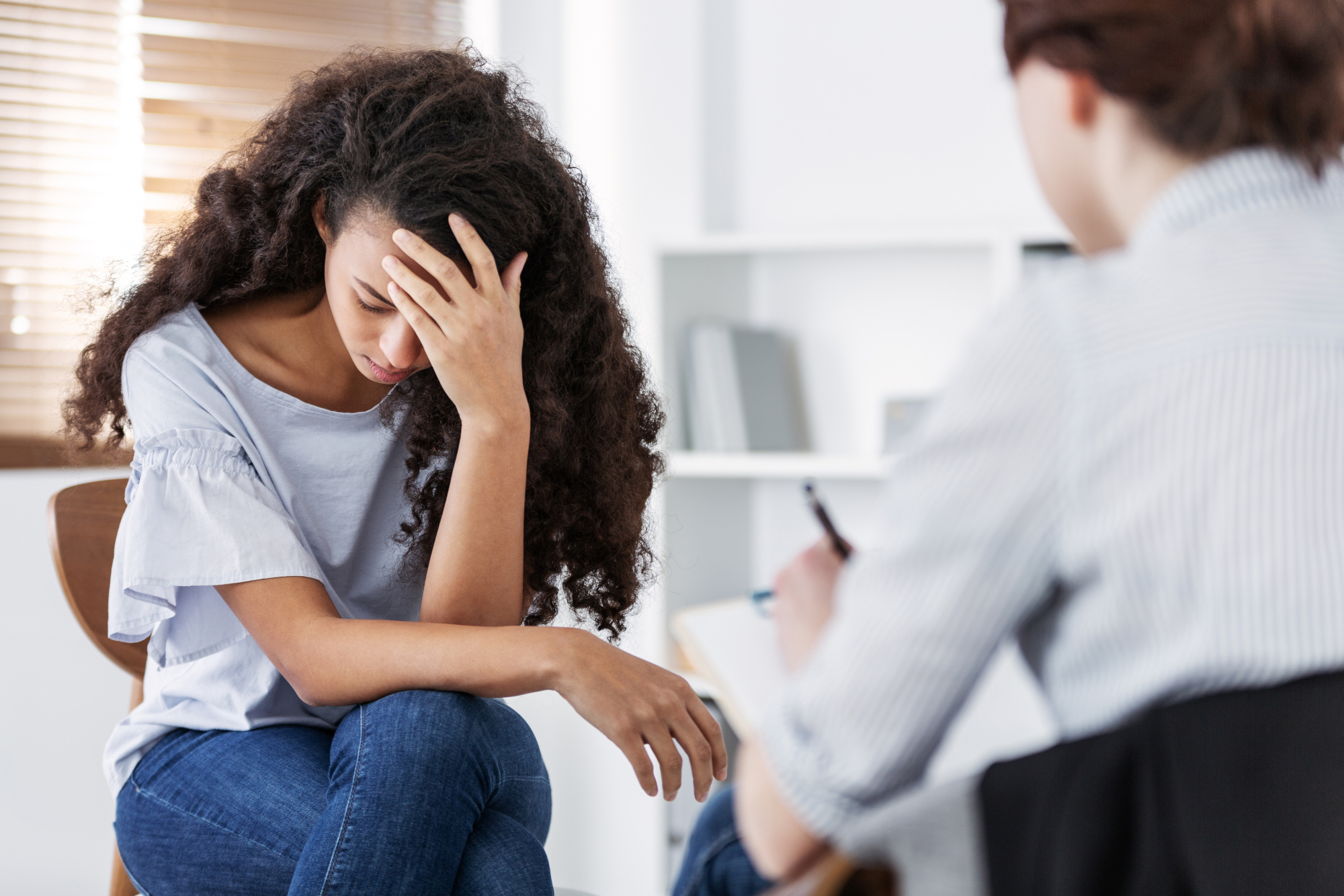 A woman is sitting in a therapists office holding her head.