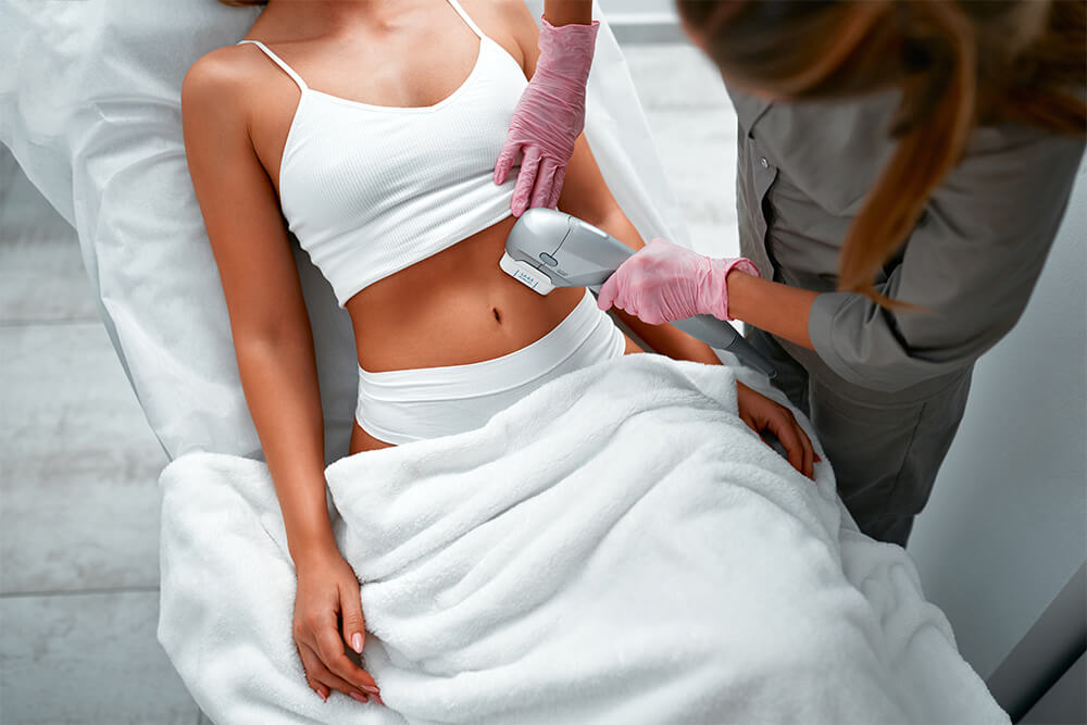 Cosmetologist using ultrasound device while performing lifting procedure on woman abdomen