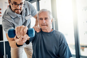 Weight, senior man and physiotherapy with clinic therapist, wellness and client assessment with dumbbell. Consultation, rehabilitation and arm exercise from physical therapy and recovery of patient