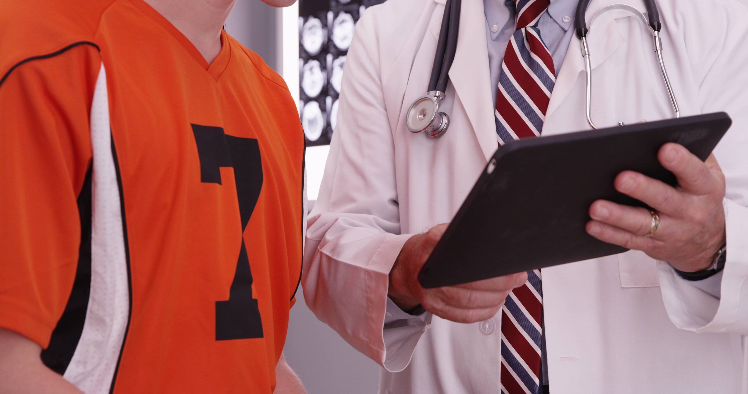 Portrait of medical doctor looking at tablet computer with college athlete.