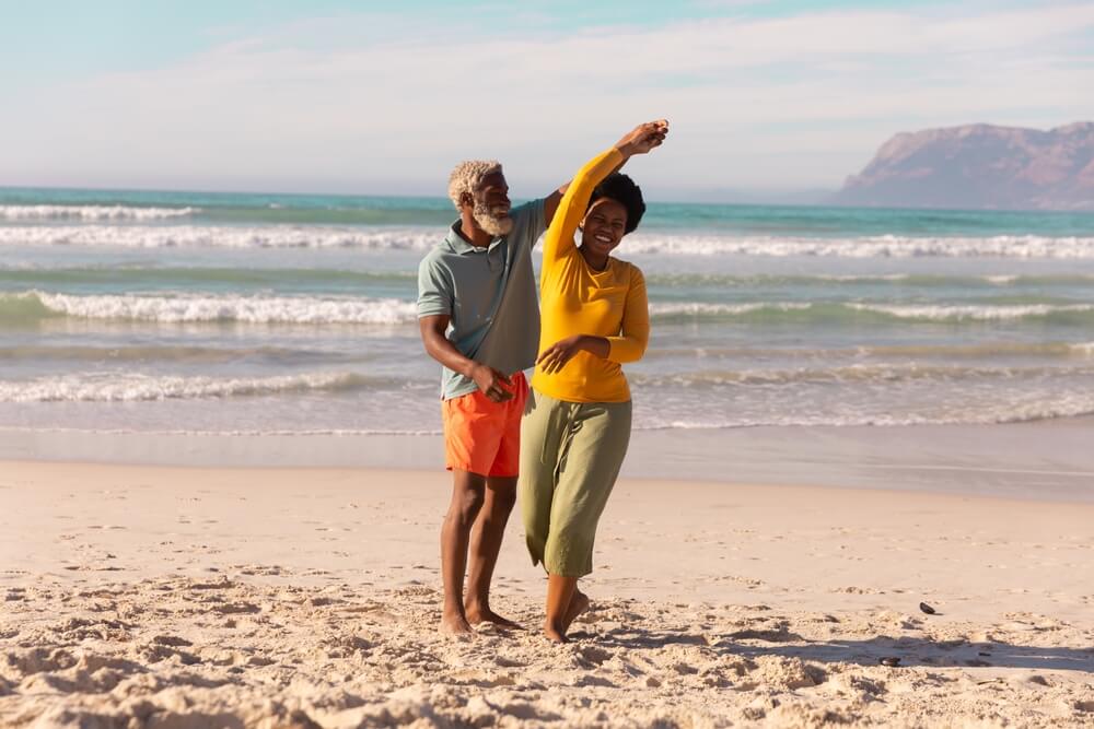 Senior man dancing with happy mature woman against sea and sky