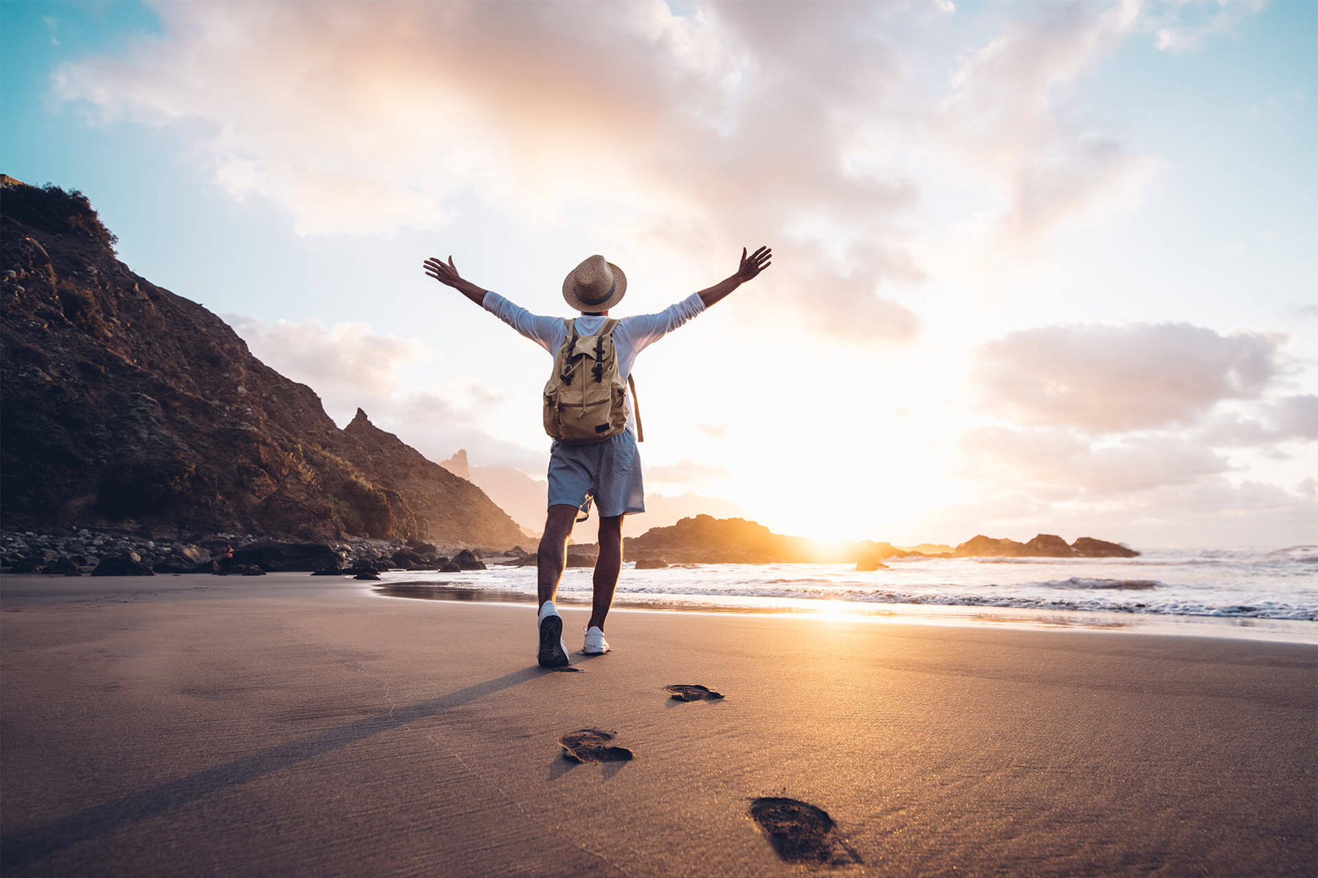 Young man arms outstretched by the sea at sunrise enjoying freedom