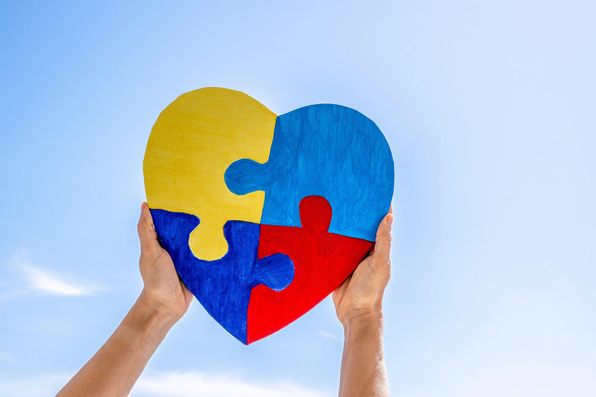 Hands holding together colorful painted puzzle heart