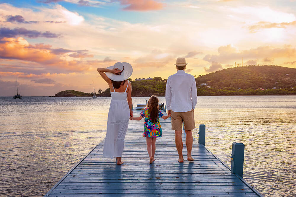 A family walks down a pier in the Caribbean sea during beautiful sunset