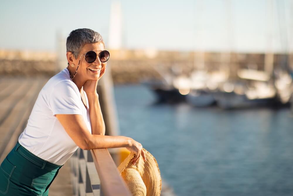 Delighted senior woman wearing her sunglasses looking at sailboats