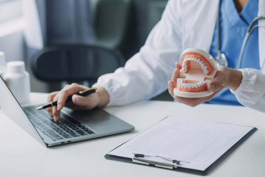 dental professional utilizing a laptop and a model of human teeth