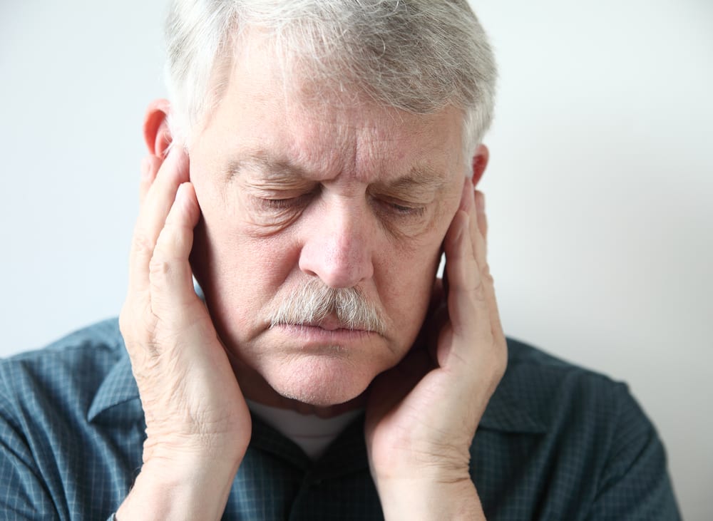 tmj, older man holds both hands to his upper jaw near the ears