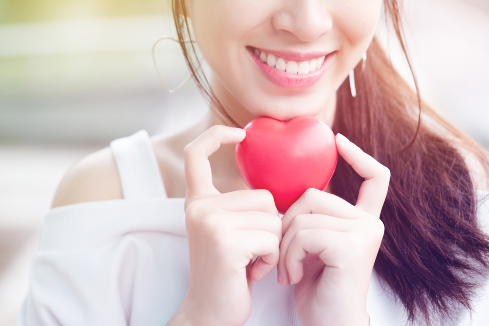 Asian teenage girls wearing white clothes smiling with a bright, relaxed, holding a red heart model represents an oral care