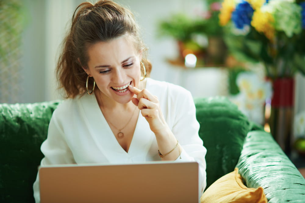 middle age housewife in white blouse speaking with dentist using tele health technology in the modern living room in sunny day.