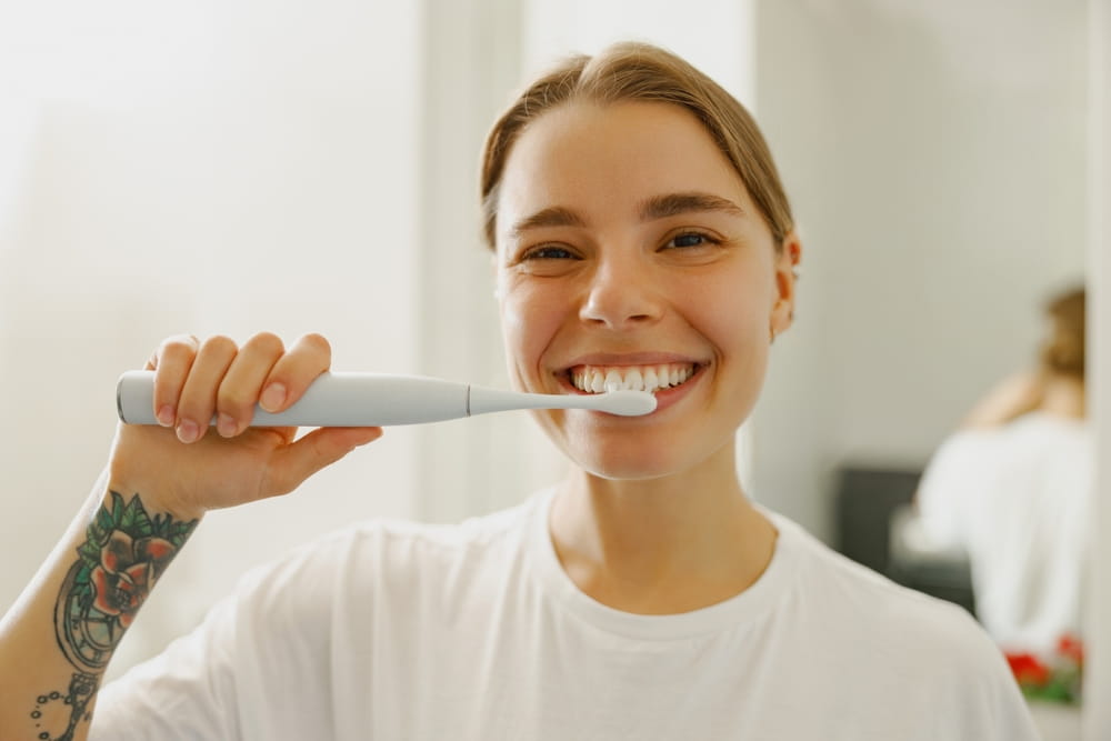 A young woman happily enjoys brushing her teeth, showcasing her bright and radiant smile in a stylish modern bathroom