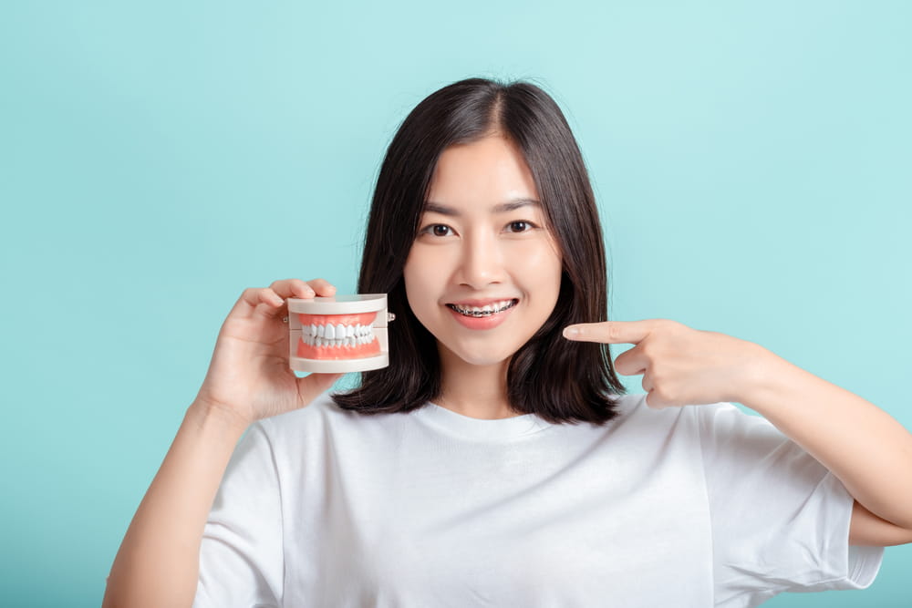 Dental braces of asian woman wearing braces with tooth sample and white teeth increase confidence f