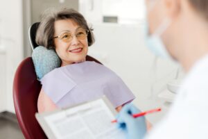 Smiling, beautiful senior woman sitting in dental chair on visit to dentist, talking in modern dentistry.