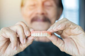 Grey haired senior man holding orthodontic prosthesis denture with a happy face standing and smiling with a confident