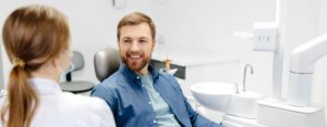 Blonde female dentist in dental office talking with male patient and preparing for treatment.