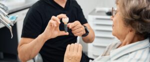 Woman examines model of dental implant in hands of dental prosthetist