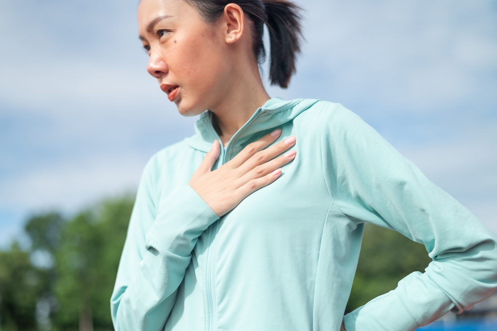 Asian female exerciser or athlete suffering from severe fatigue and chest pain