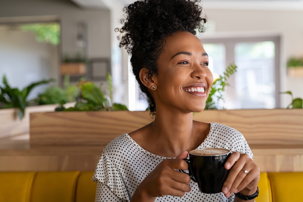 Carefree african american woman sitting in cafeteria drinking coffee while looking away