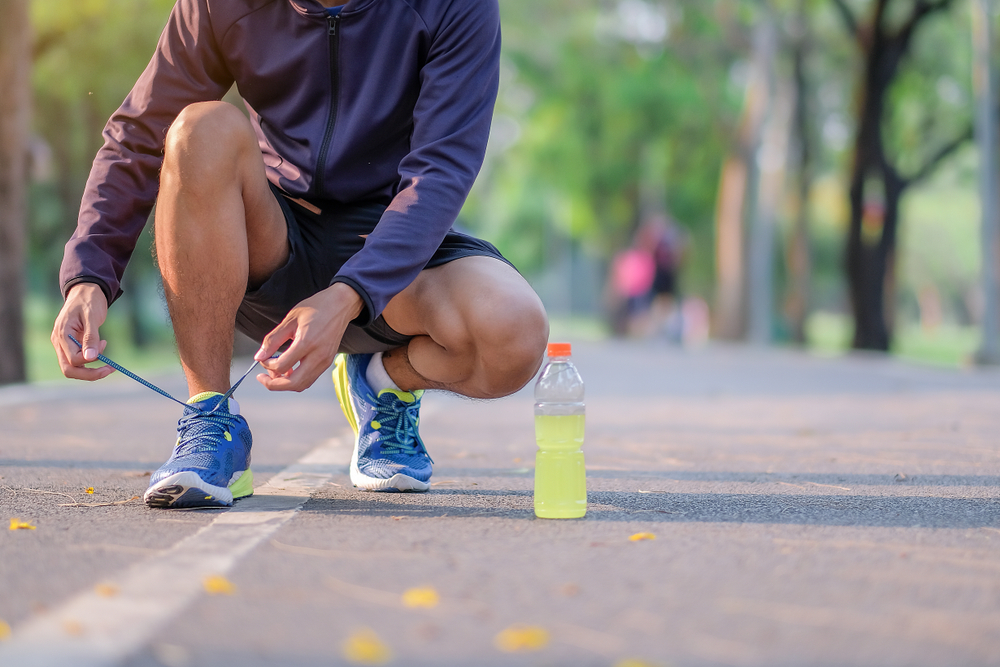 Young athlete man tying running shoes in the park outdoor, male runner ready for jogging on the road outside