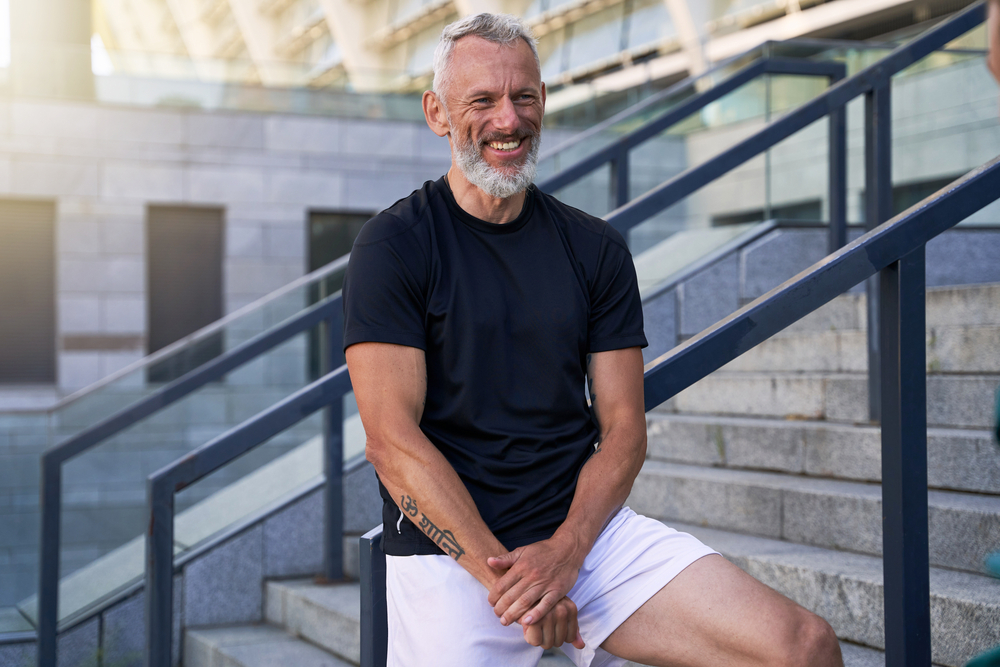 Cheerful middle aged man in perfect shape smiling at camera while posing, standing outdoors in the city
