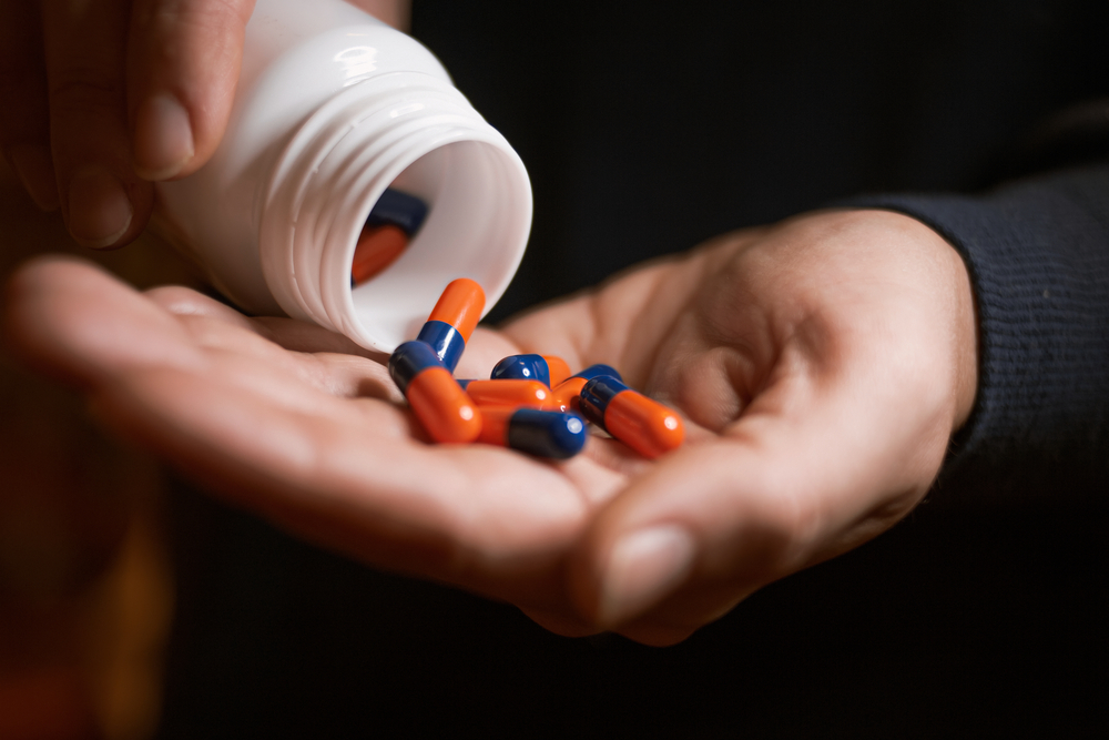 Mans hands with pills on, spilling pills out of bottle on dark background