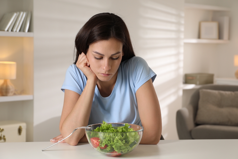 Eating disorder. Sad woman near bowl with salad