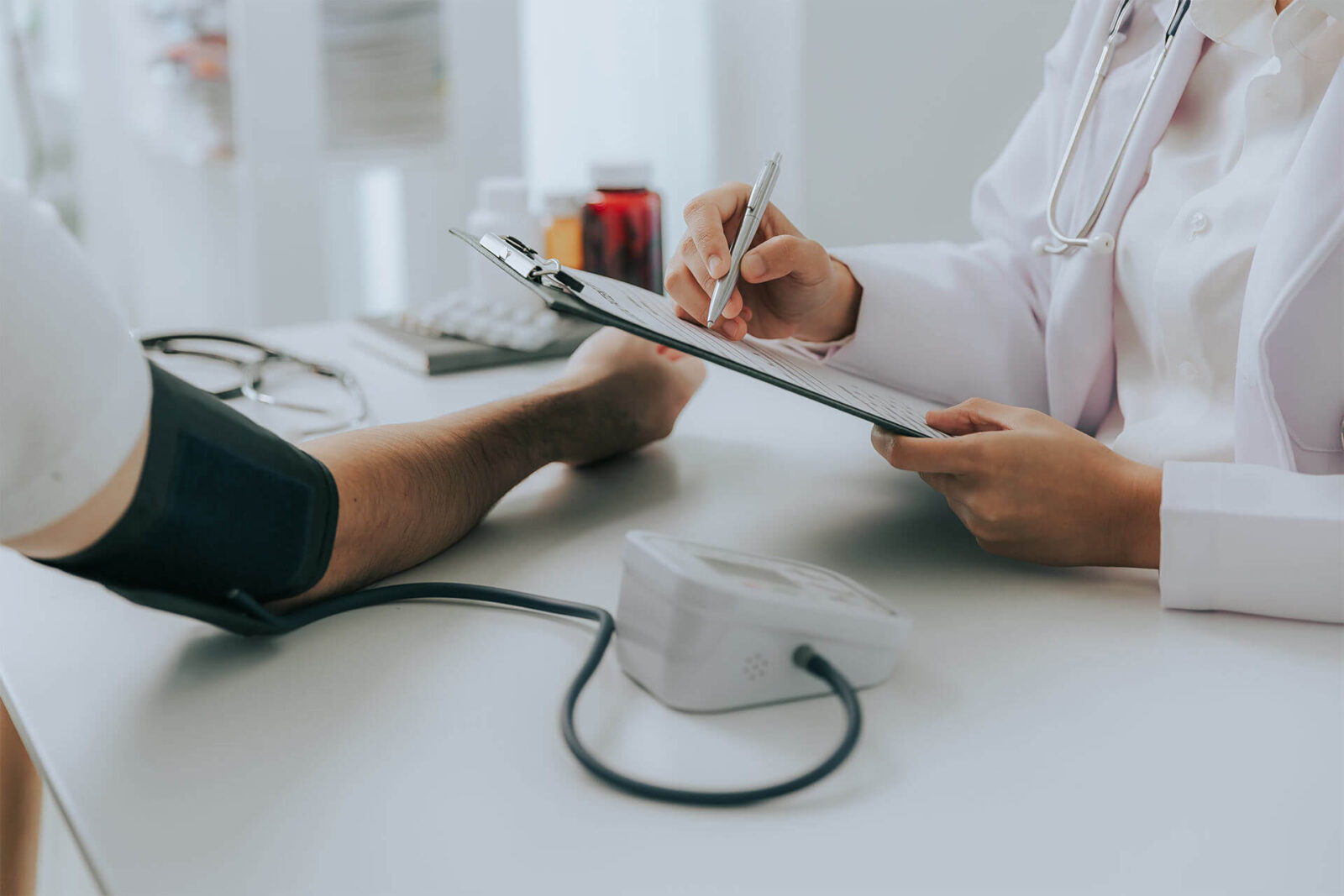 Female doctor's hands using a blood pressure monitor and stethoscope to check blood pressure on a sick man in hospital