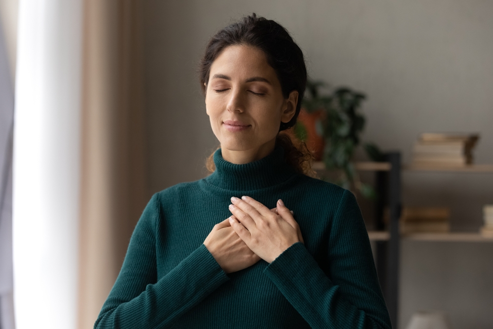young attractive woman holding folded hands on chest, praying