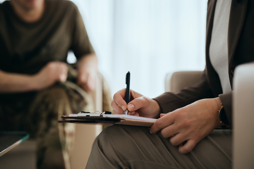 Close-up of mental health professional writing notes while having meeting with a veteran.