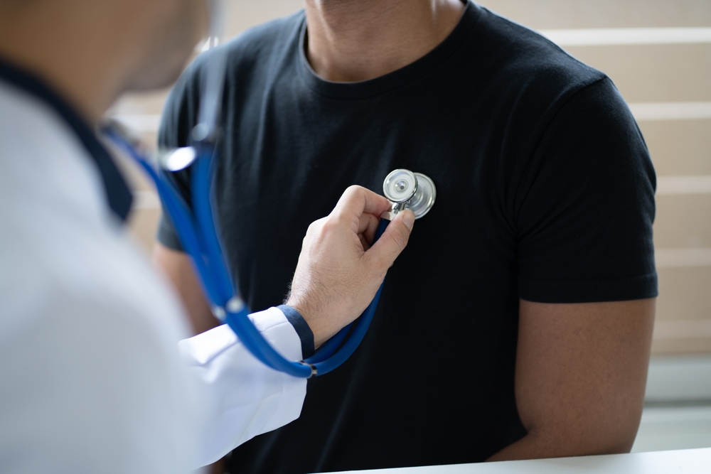 Young male doctor holding stethoscope examining his male patient in the clinic room