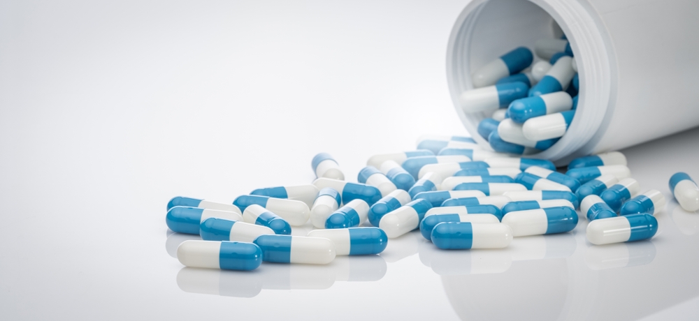 Blue-white antibiotic capsule pills spread out of plastic drug bottles