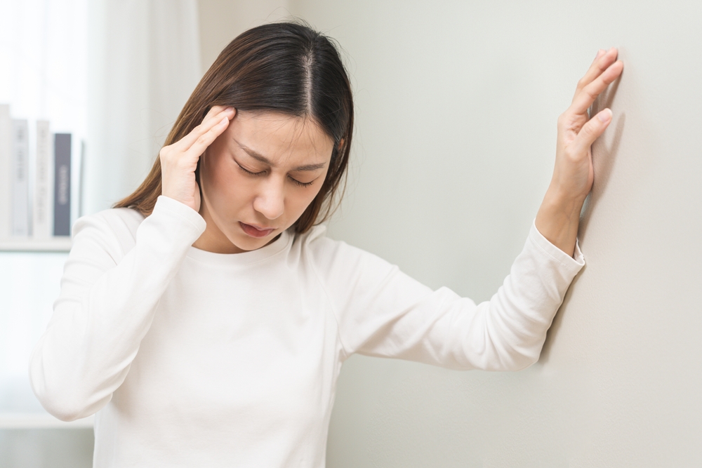 Dizzy asian young woman, girl headache or migraine pain. suffering from vertigo, difficulty standing up leaning on wall at home