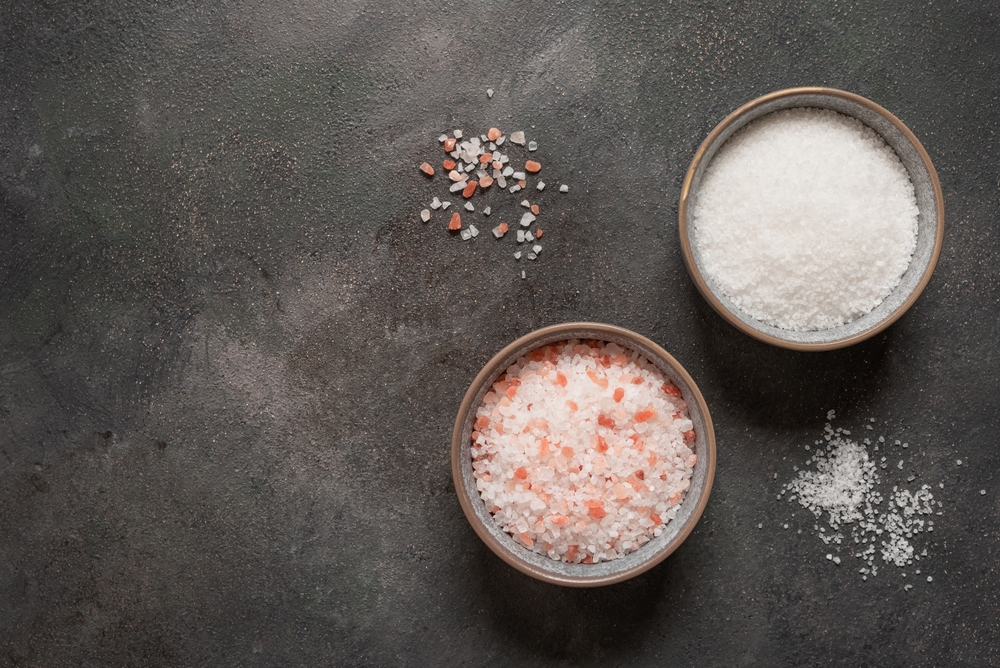 Pink himalayan salt and sea salt in bowls on dark rustic backgroun