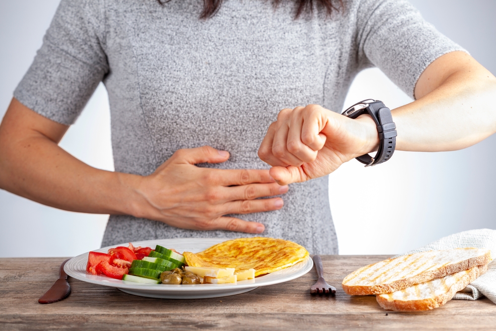 woman sitting hungry in front of food and looking at her watch to make sure she breaks fast on the correct time.