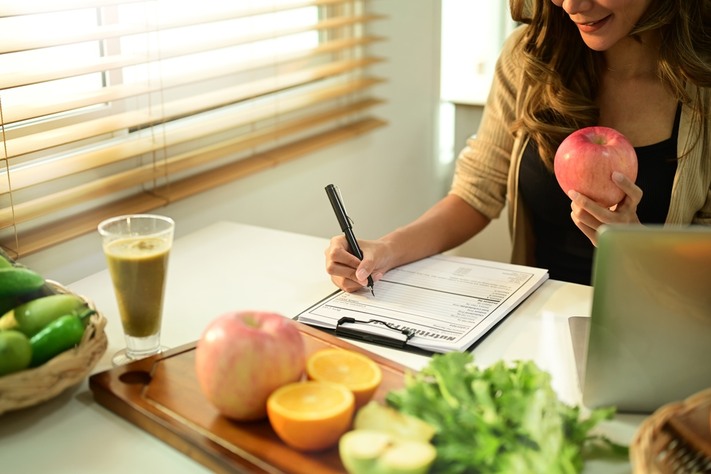 Nutritionist sitting at desk with fruit and vegetable, working on diet plan