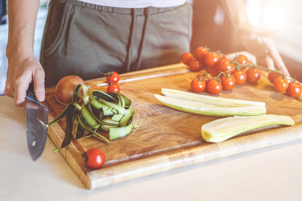 Female hand holding knife for cutting colorful fresh vegetables on a wooden board