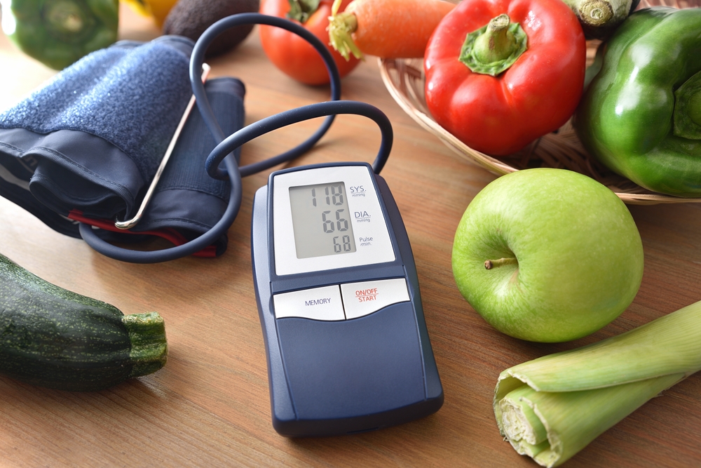 Healthy eating for blood pressure control with blood pressure monitor on wooden kitchen bench and fruits and vegetables around.