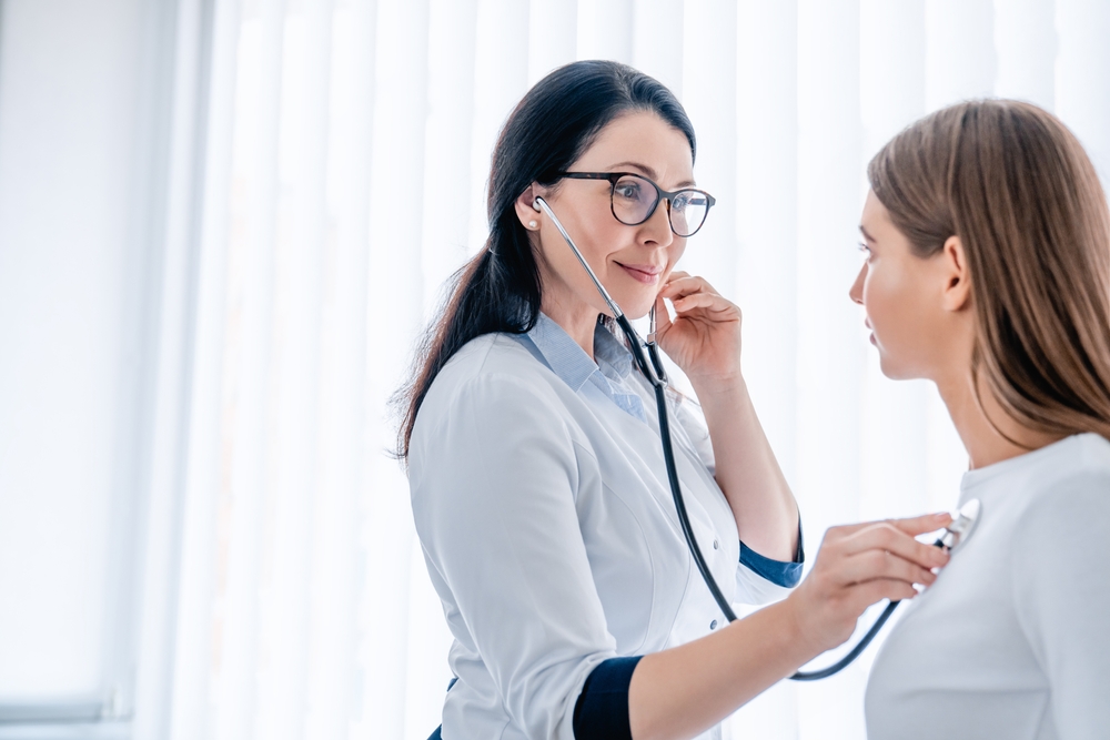 Female doctor listening to patients chest with stethoscope at the hospital, checking on lungs illnesses diseases
