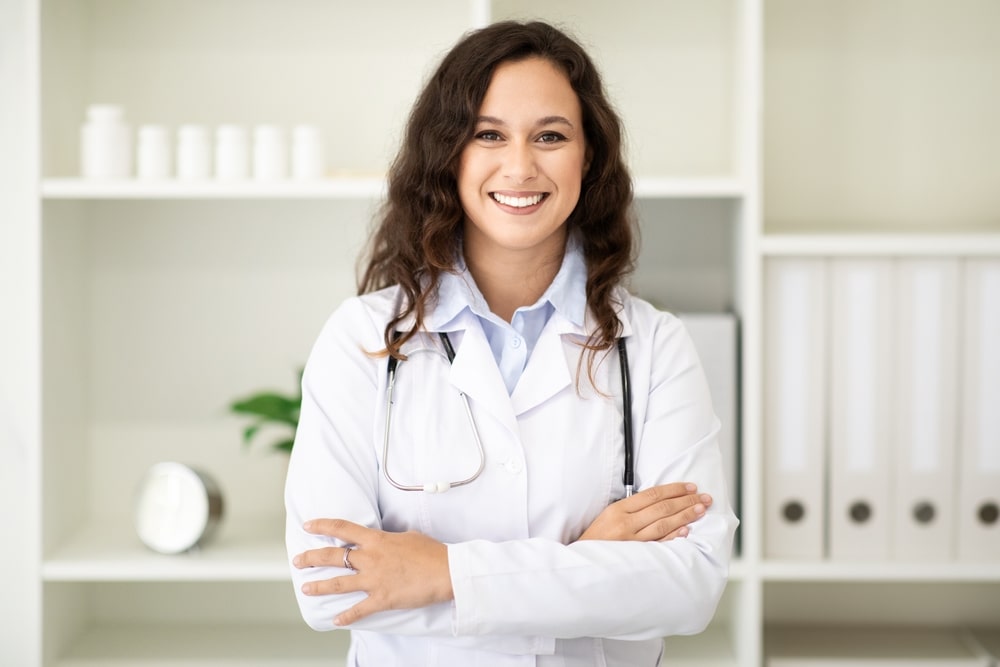 Private medical practice. Portrait of friendly beautiful long-haired brunette millennial woman wearing medical coat doctor posing at clinic