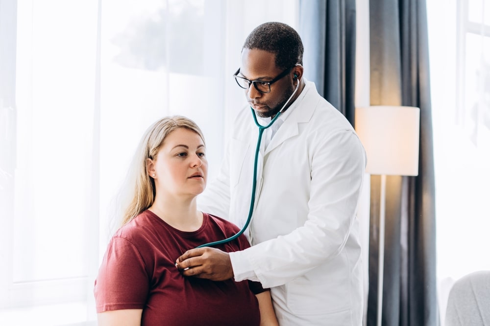 African American doctor checking heart, lungs and breathing test of female patient in hospital. Healthcare and cardiology concept