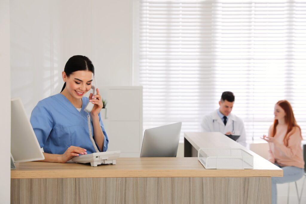 Receptionist talking on phone while doctor working with patient