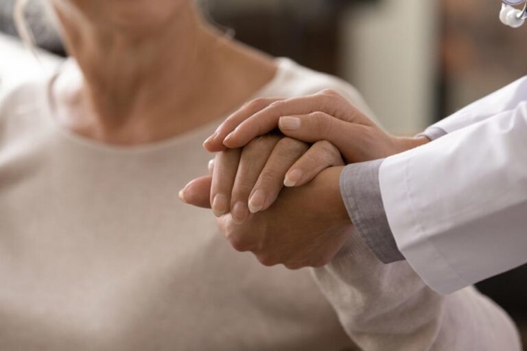 Female doctor in white coat holding hand of senior patient,