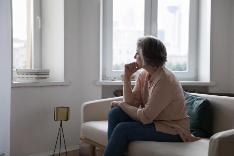 Sad lonely mature grey haired lady looking at window