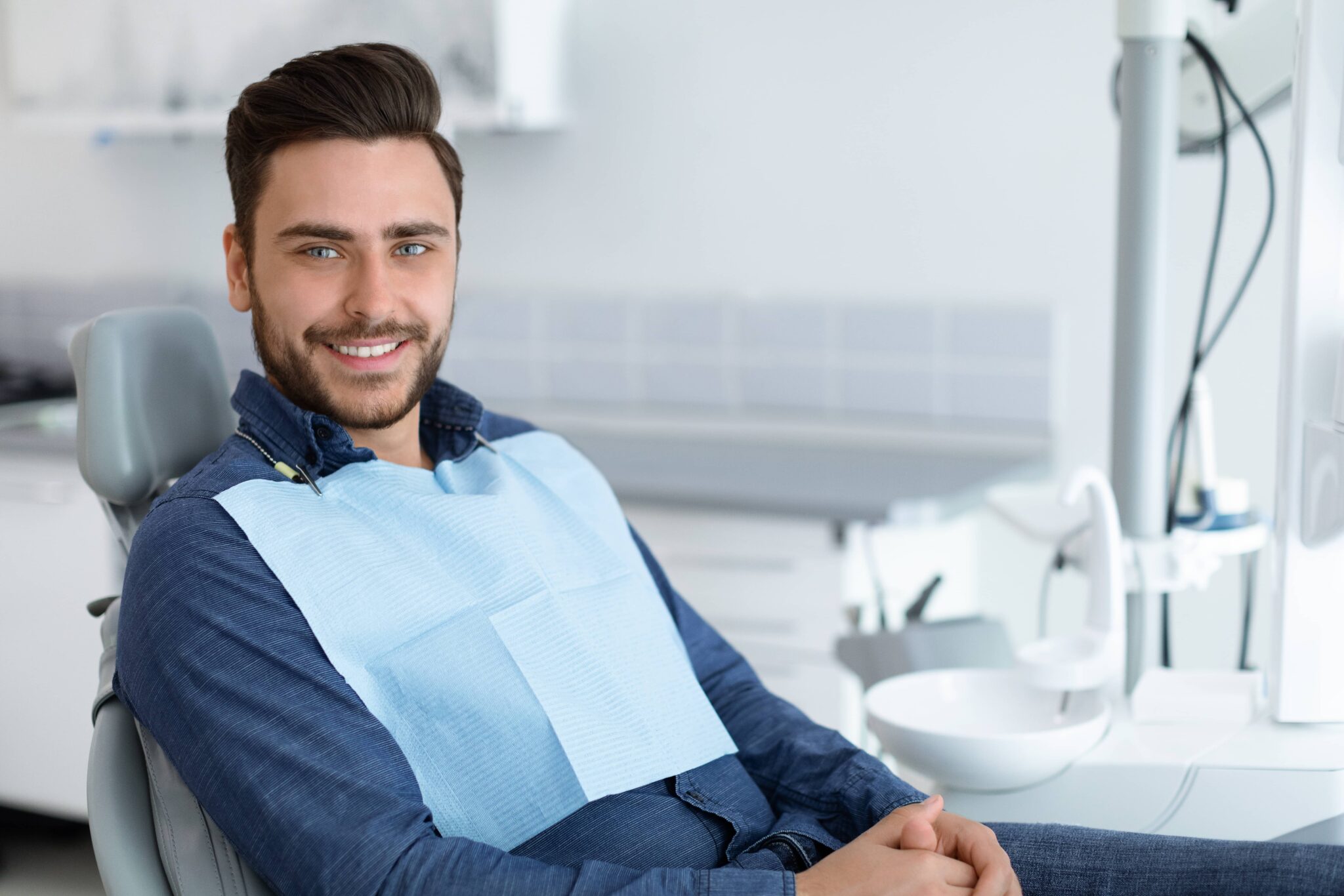 Side view of handsome young man patient sitting in dental chair and smiling, panorama with copy space