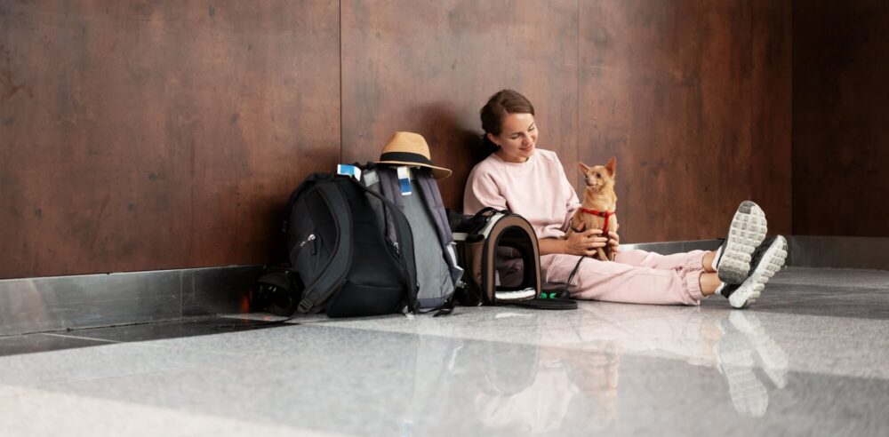 Young adult woman travelling with her small dog sitting on floor