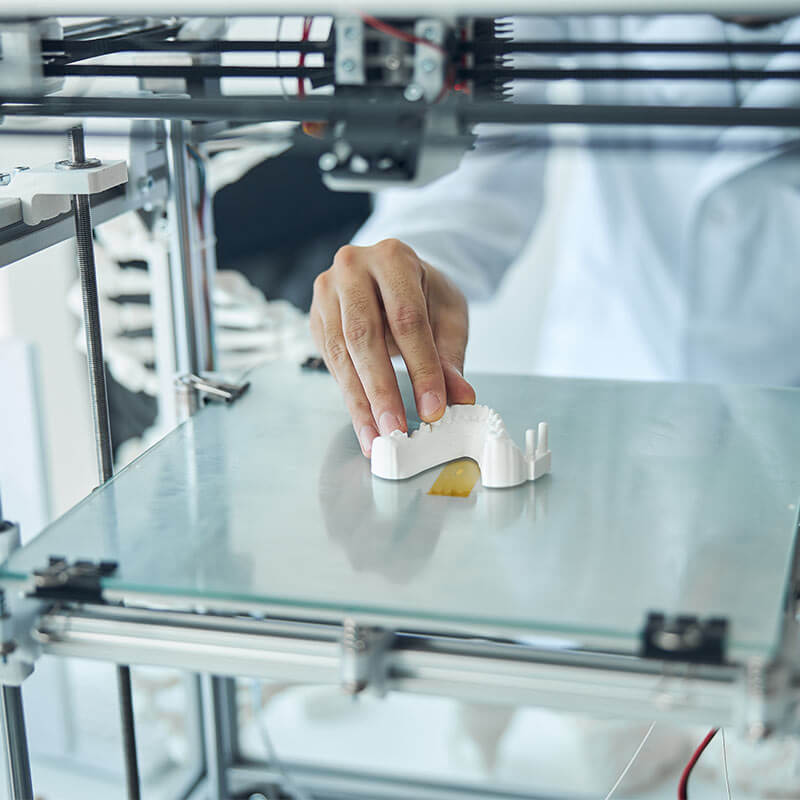 person handling a 3D-printed dental prosthetic, likely a denture or part of one, on the build plate of a 3D printer