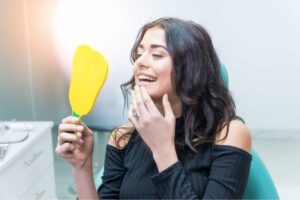 woman in a dentist chair checking her teeth in a mirror